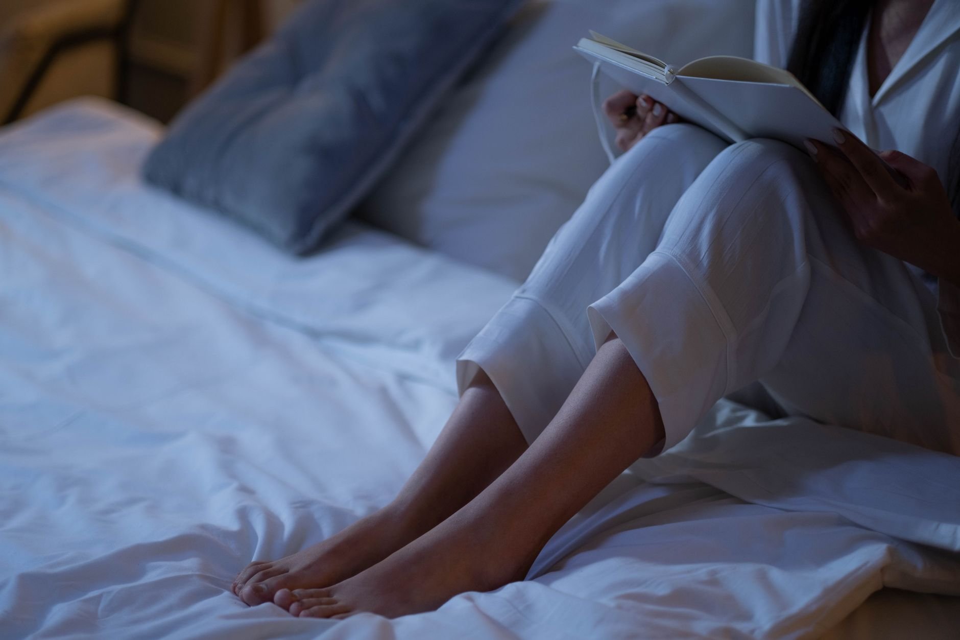 Woman relaxing in bed with a book on a calm evening — the unhurried approach to sleep we believe in